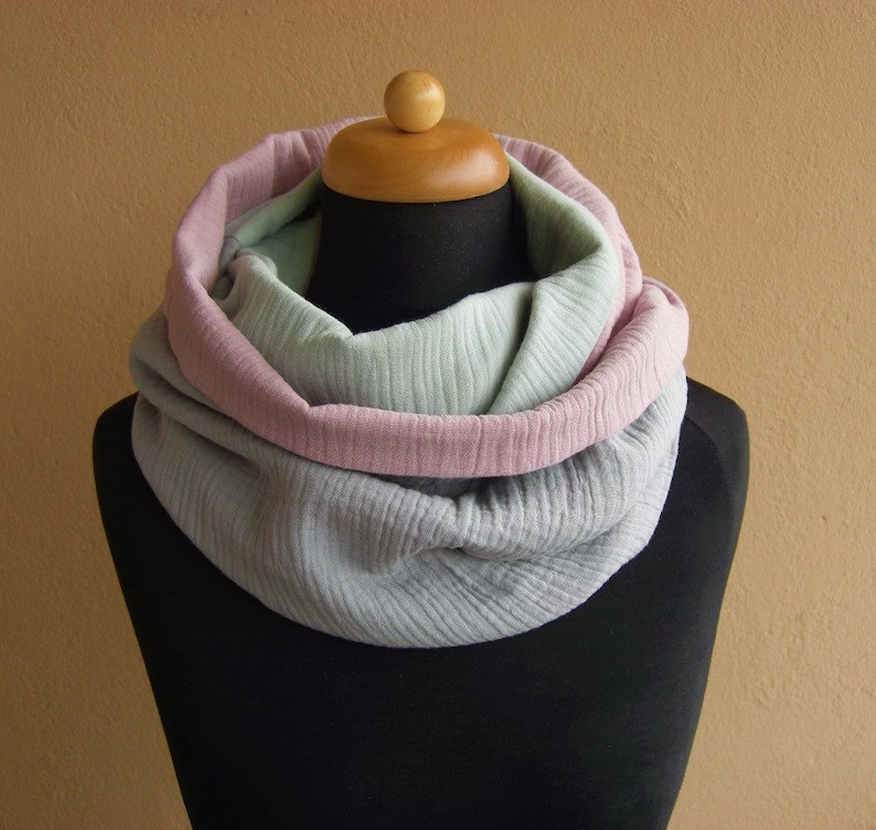 May include: A soft, cozy infinity scarf in shades of gray, pink, and green. The scarf is made of a lightweight fabric and is perfect for layering in the cooler months.