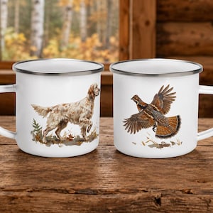 Könnte beinhalten: Zwei weiße Emaille-Tassen mit silbernen Rändern. Die linke Tasse zeigt einen braun-weiß gefleckten Jagdhund, der im Gras steht. Die rechte Tasse zeigt einen braun-schwarzen Wildvogel im Flug mit weit ausgebreiteten Flügeln über einem Stück Boden.