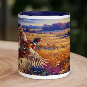 Könnte beinhalten: Ein Keramikbecher mit dunkelblauem Innenraum und Rand, der eine lebendige, texturierte Ölgemälde-Illustration eines fliegenden Fasans über einem goldenen Feld mit violettem und blauem Himmel sowie Bäumen im Hintergrund zeigt.