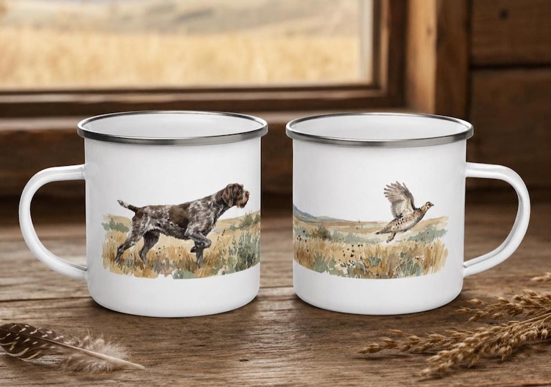 K&ouml;nnte beinhalten: Zwei wei&szlig;e Emaille-Tassen mit silbernen R&auml;ndern und Henkeln. Eine Tasse zeigt einen braun-wei&szlig;en Deutsch Kurzhaar Hund auf einem Feld. Die andere Tasse zeigt einen braun-wei&szlig;en Wildvogel im Flug &uuml;ber einer grasbewachsenen Landschaft.