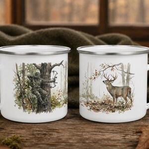 May include: Two white enamel mugs with silver rims. The left mug features a watercolour illustration of a person in camouflage clothing using a compound bow in a tree. The right mug displays a watercolour illustration of a deer in a forest.