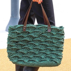 May include: A green crocheted tote bag with brown leather handles. The bag has a unique, textured design.