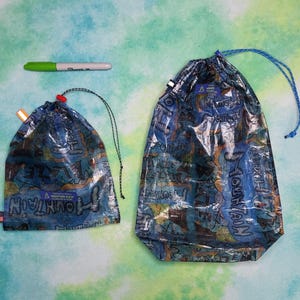 May include: Two drawstring bags with a blue and tan map design. The bags have blue drawstrings and are made of a lightweight, waterproof material. A green and white Sharpie marker is above the bags.