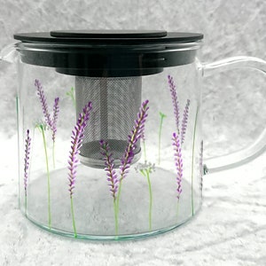 Puede incluir: Una tetera de vidrio transparente con tapa negra y un infusor de malla de acero inoxidable. La tetera est&aacute; decorada con un dise&ntilde;o floral de lavanda.
