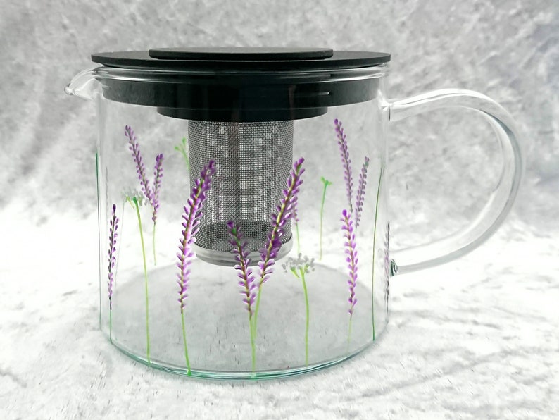 Puede incluir: Una tetera de vidrio transparente con tapa negra y un infusor de malla de acero inoxidable. La tetera est&aacute; decorada con un dise&ntilde;o floral de lavanda.