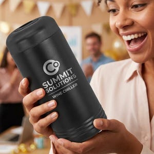 May include: A black wine chiller with the text "SUMMIT SOLUTIONS WINE CHILLER" in white. The cylindrical cooler is held by a person in a light pink shirt. The background is blurred, suggesting a social gathering.