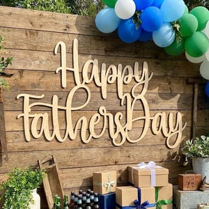 May include: Wooden sign that reads "Happy Father's Day" in cursive script, mounted on a rustic wooden wall. The scene is decorated with balloons in shades of blue, green, and white, and gift boxes.