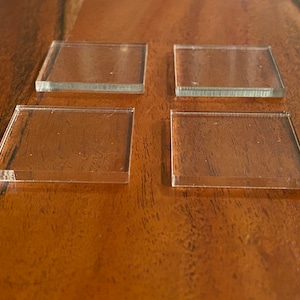 May include: Four clear acrylic squares on a wooden surface.