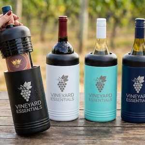 May include: A selection of wine bottle coolers in black, white, teal, and navy blue, each with a black top. The coolers feature the text "VINEYARD ESSENTIALS" and a grape cluster design. One cooler is being held, revealing a wine bottle.