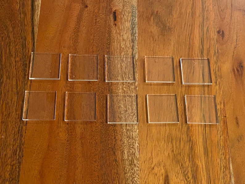 Puede incluir: Diez cuadrados de acr&iacute;lico transparente dispuestos en dos filas de cinco sobre una superficie de madera.