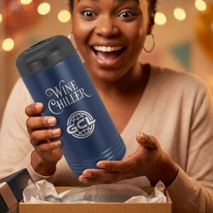 May include: A navy blue wine chiller with a black top is held by a person. The text "Wine Chiller" and a logo are printed on the side. The person is opening a gift box.