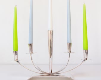 May include: A silver candelabra with five candles. The candles are in shades of white, light blue, and green. The candelabra has a modern design with a curved base and holders for the candles.