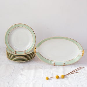 Könnte beinhalten: Ein Set aus Vintage-Porzellantellern und einer Servierplatte mit mintgrünem und goldenem Rand. Die Teller sind gestapelt, die Platte ist oval. Das Set steht auf einer weißen Tischdecke.
