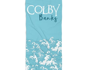 May include: A light blue beach towel with a white wave pattern and the text "COLBY Banks" in white.