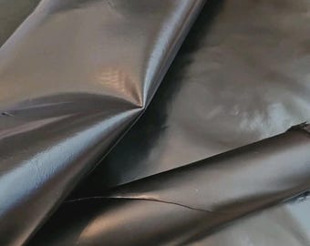 May include: A close-up of a roll of black leather. The leather has a glossy finish and is folded over itself, revealing the underside. The edges of the leather are slightly frayed. The leather is likely used for crafting.