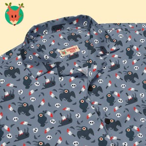 May include: A slate blue button-down shirt featuring an all-over pattern of dark gray birds, white skulls, and silver knives with red blood stains. The shirt has a notched collar and a small rectangular label reading Scribble Root at the neck.