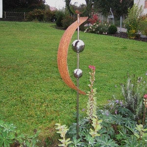 Könnte beinhalten: Eine hohe Metallskulptur für den Außenbereich mit einer polierten silbernen Kugel an der Spitze und zwei kleineren Kugeln darunter. Ein gebogenes, braunes, strukturiertes Element fügt ein einzigartiges Design hinzu. Die Skulptur steht in einem grünen Garten.