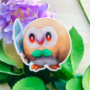 May include: A brown and white owl Pokemon sticker with red eyes and a green mouth holding a silver knife.