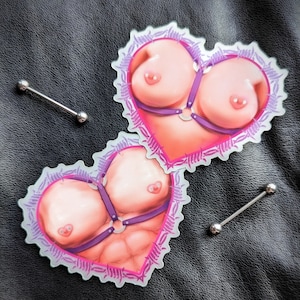 Peut inclure: Deux autocollants en forme de cœur avec une bordure de fil barbelé. Chaque autocollant présente une illustration nue d'un torse avec un harnais violet. Le harnais a un anneau au centre.