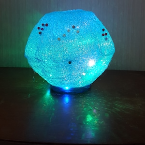 May include: A blue, glittery, spherical lamp with red and silver accents. The lamp is lit and casting a blue glow.