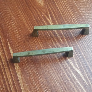 Puede incluir: Dos tiradores de armario de metal de estilo antiguo con acabado cepillado. Los tiradores son rectangulares con bordes redondeados y tienen un diseño simple y minimalista.