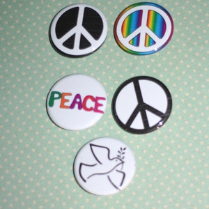 May include: Five peace sign buttons. One button is black and white, one is rainbow colored, one says "PEACE" in rainbow colors, one is black and white with a peace sign, and one is white with a dove and an olive branch.