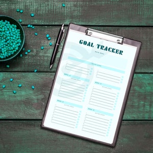 May include: A black clipboard with a white goal tracker sheet. The sheet has a section for a main goal and five sections for smaller goals. Each goal section has a space for action steps and a checklist.