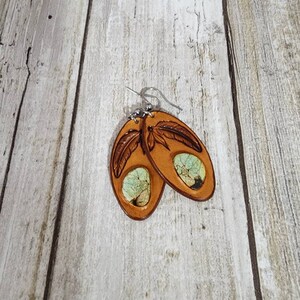 May include: A pair of brown leather earrings with a turquoise inlay and a carved feather design.