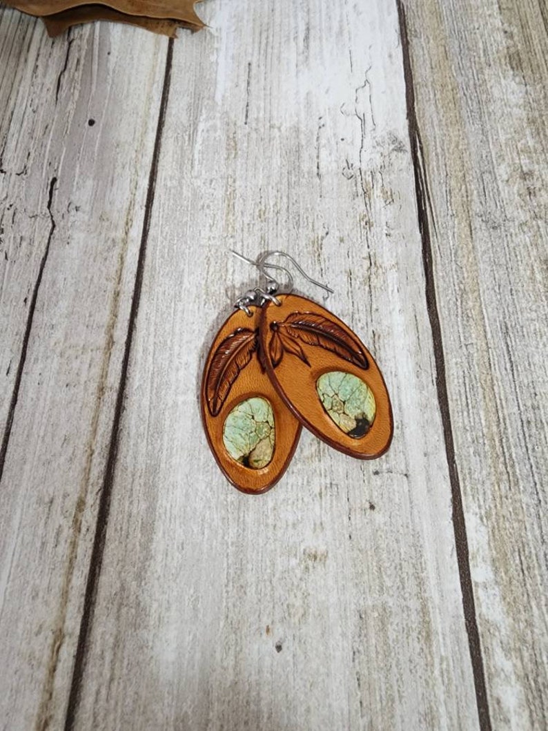May include: A pair of brown leather earrings with a turquoise inlay and a carved feather design.
