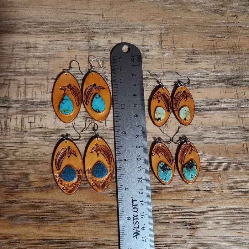 May include: Six pairs of leather earrings with turquoise stones. The earrings are oval shaped and have a feather design.