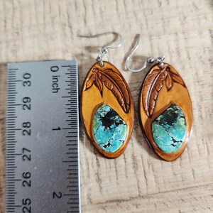 May include: A pair of leather earrings with turquoise stones and a carved feather design. The earrings are approximately 1 inch long.