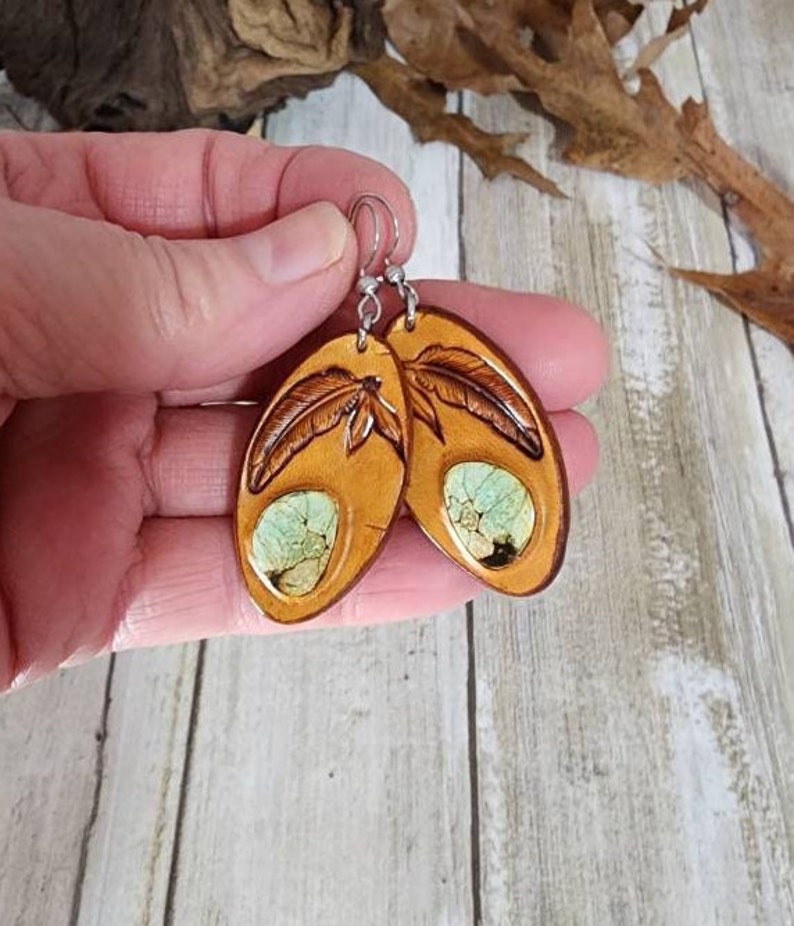 May include: A pair of brown leather earrings with a green and white stone inlay and a carved feather design.