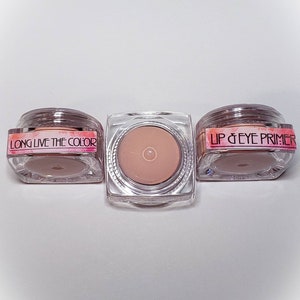 Puede incluir: Tres pequeños frascos transparentes con tapas blancas. Los frascos contienen una crema rosa claro. Las etiquetas en los frascos dicen "Long Live The Color" y "Lip & Eye Primer".
