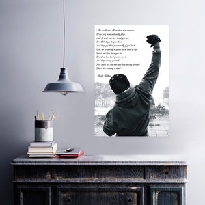 May include: A black and white print of a man with his fist raised in the air, with a quote from Rocky Balboa. The quote is in a white font and reads, "The world ain't all sunshine and rainbows..." The image is displayed on a white wall.