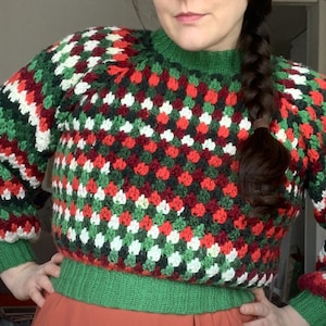 Może przedstawiać: Zielony, czerwony, biały i czarny sweter na szydełku z geometrycznym wzorem.