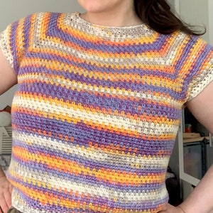 Pode incluir: Um top de crochê com um padrão listrado em tons de roxo, laranja, amarelo e branco.