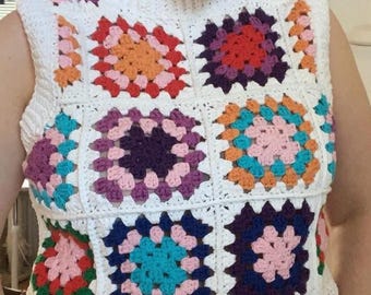 Può includere: Un top bianco senza maniche all'uncinetto con un motivo a quadrati della nonna colorati. I quadrati sono realizzati in tonalità di rosso, arancione, rosa, viola, blu, verde e bianco.