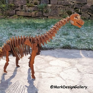 Könnte beinhalten: Eine rostige Metall-Dinosaurierskelett-Skulptur in einer Gartenlandschaft. Die Skulptur steht auf einem Steinweg mit einer grasbewachsenen Fläche im Hintergrund. Die Skulptur ist aus Metall gefertigt und hat eine rostige Oberfläche. Die Skulptur ist etwa 90 cm hoch und 150 cm lang.
