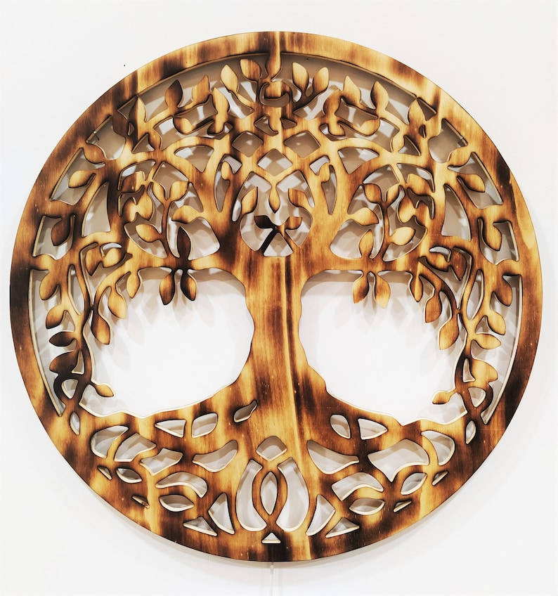 May include: A circular wooden wall decor with a detailed cutout design of a tree of life. The tree has intricate branches and roots, and the wood has a natural, burnt finish.