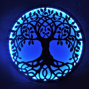 May include: A circular wooden wall decor with a black silhouette of a tree of life with intricate branches and roots. The background is a bright blue color with a light blue border.