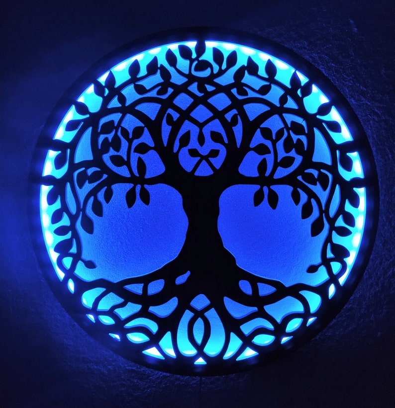 May include: A circular wooden wall decor with a black silhouette of a tree of life with intricate branches and roots. The background is a bright blue color with a light blue border.