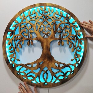 May include: A circular wooden wall decor with a cutout design of a tree of life. The tree is illuminated with blue LED lights.