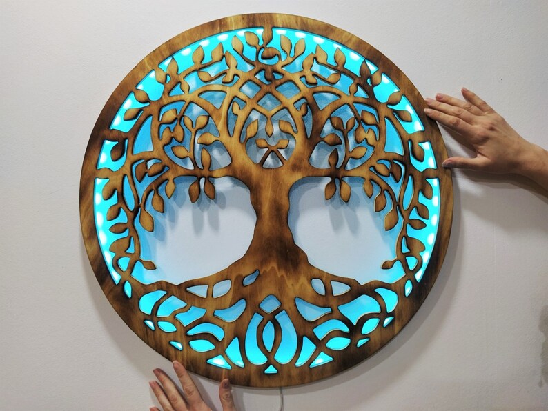May include: A circular wooden wall decor with a cutout design of a tree of life. The tree is illuminated with blue LED lights.