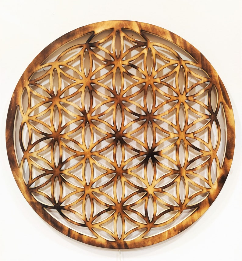 May include: A wooden wall hanging in the shape of a circle with a geometric pattern of overlapping circles and triangles. The pattern is carved into the wood and the wood is a light brown color.