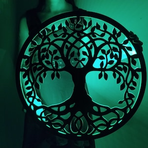 May include: A black wooden tree of life wall decor with intricate branches and roots, illuminated by a green light.