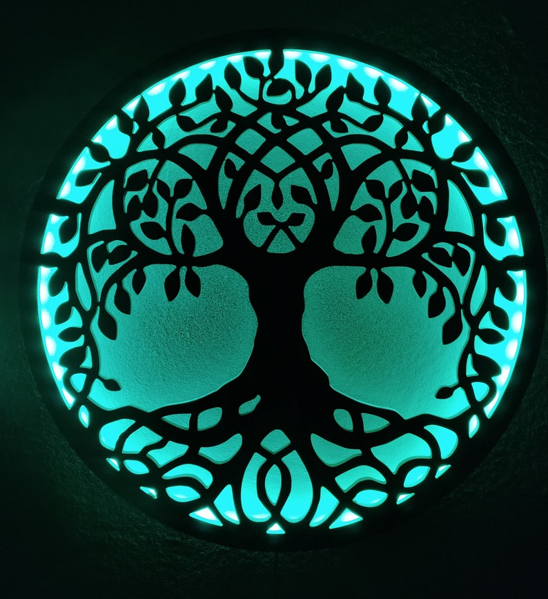 May include: A circular wooden wall decor with a cutout design of a tree of life. The tree is black and the background is a teal blue color.