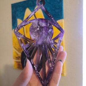 May include: A purple and white diamond-shaped ornament with a galaxy-like design inside. The ornament is made of resin and has a sparkly finish.
