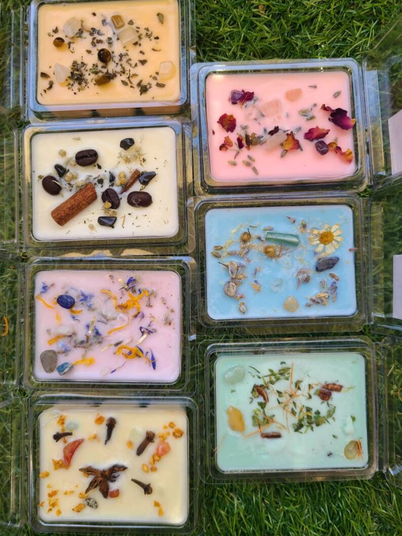 K&ouml;nnte beinhalten: Sortiment von sechs kleinen quadratischen Wachs-Schmelzen in durchsichtigen Plastikbeh&auml;ltern. Die Wachs-Schmelzen sind in verschiedenen Farben, darunter hellorange, rosa, hellblau und gr&uuml;n. Jede Wachs-Schmelze enth&auml;lt verschiedene nat&uuml;rliche Elemente, die in das Wachs eingebettet sind, wie z. B. getrocknete Blumen, Kr&auml;uter und Kristalle.