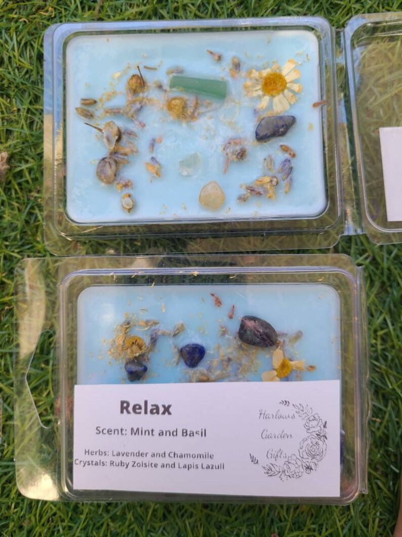 K&ouml;nnte beinhalten: Ein blaues Wachs-Melt mit getrockneten Blumen und Kristallen. Das Etikett lautet "Relax" mit dem Duft "Minze und Basilikum", Kr&auml;utern "Lavendel und Kamille" und Kristallen "Rubinzoisit und Lapislazuli". Das Etikett enth&auml;lt auch den Text "Harlows Garden Gifts".