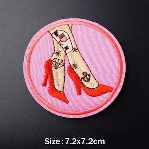 Peut inclure: Écusson brodé représentant des jambes chaussées de talons hauts rouges avec des tatouages, sur fond rose dans un cadre circulaire. Le patch mesure 7,2 x 7,2 cm.